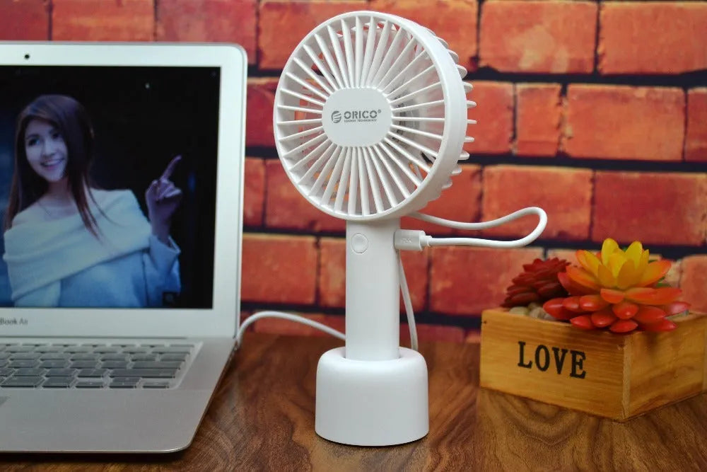 White ORICO FH1 handheld USB rechargeable desk fan with three-speed buttons on a desk.