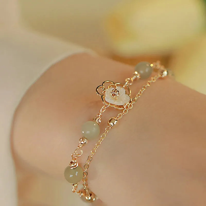 Yellow gold electroplated copper women's bracelet with geometric design showing butterfly and shell flower charms including Hetian jade elements