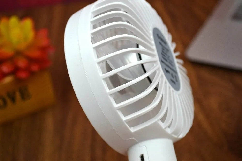 White ORICO FH1 handheld USB rechargeable desk fan with three-speed buttons on a desk.