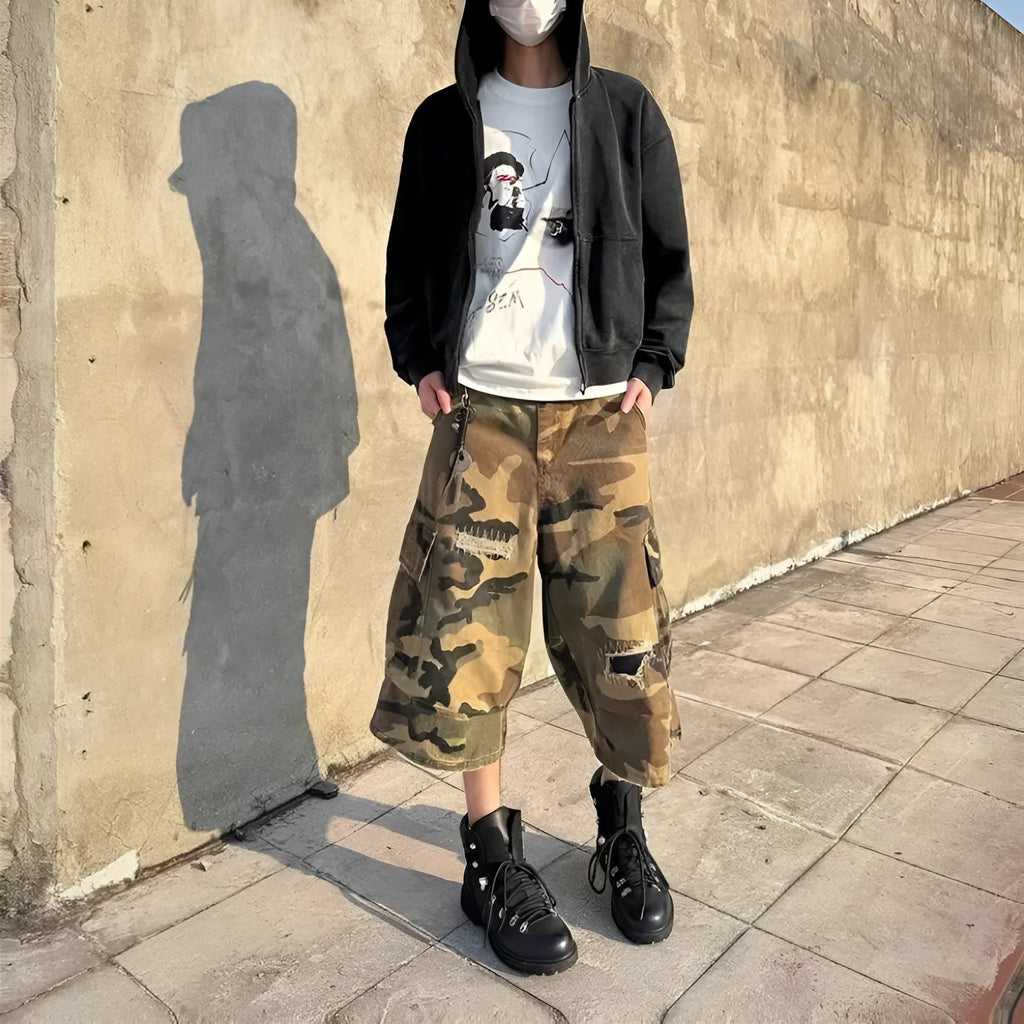 Man wearing loose fit camouflage print cropped jeans with ripped knees and patchwork details.