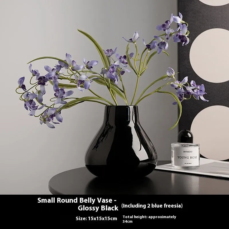 Black ceramic modern vase with white artificial orchid stems on wooden table