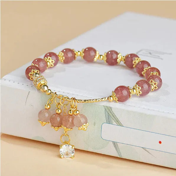 Close-up of a women's pink crystal bracelet with a heart-shaped Strawberry Quartz stone and a white pearl accent.