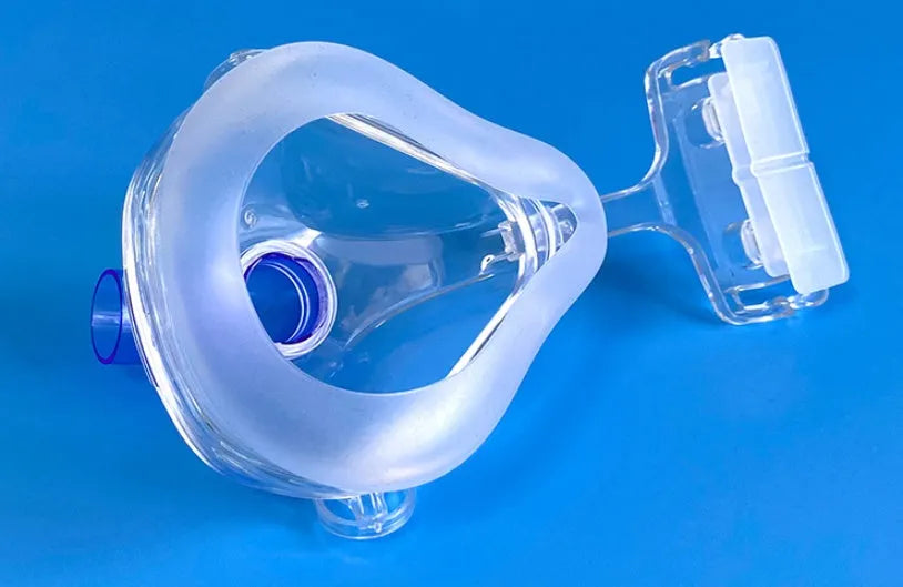 Transparent silicone CPAP breathing mask with headband and two adapter elbows on a white background.