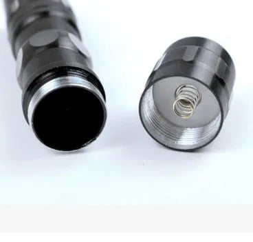 Small black aluminium LED flashlight showing compact size next to a AA battery for scale.