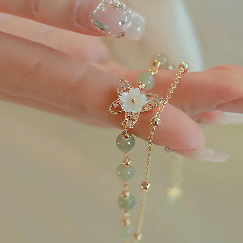 Yellow gold electroplated copper women's bracelet with geometric design showing butterfly and shell flower charms including Hetian jade elements