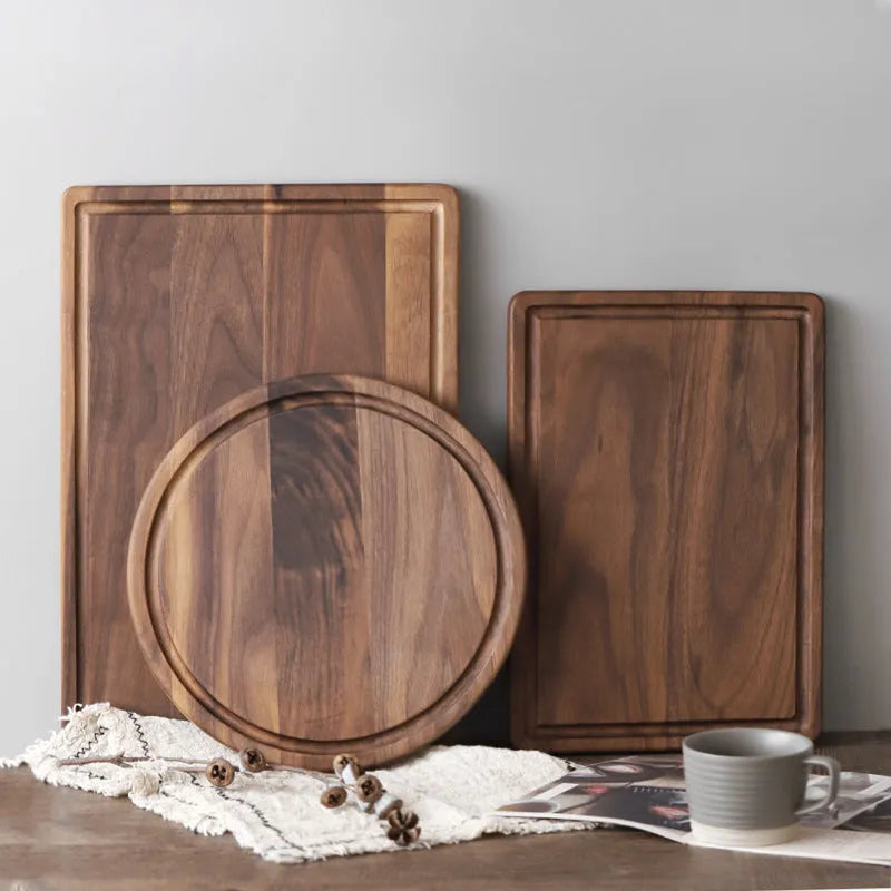 Black walnut wood chopping board with juice groove and side handle on kitchen counter