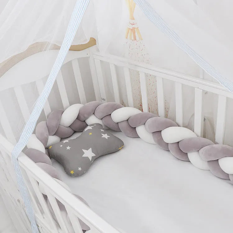 Braided knot design crib bumper in spandex velvet, shown in a light grey colour wrapped around crib slats.
