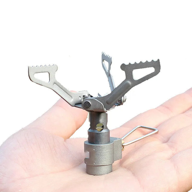 Portable camping gas stove with one-piece furnace on a rocky outdoor surface.