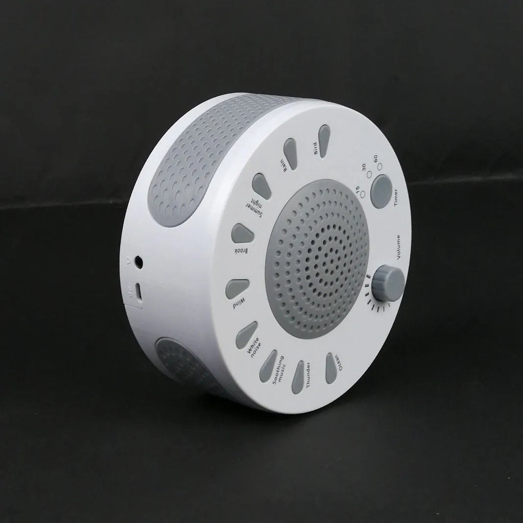 White noise sleep machine with volume knob, showing white colour option, beside USB cable on table