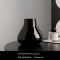 Black ceramic modern vase with white artificial orchid stems on wooden table