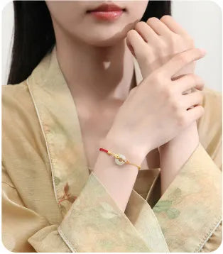 Gold and red women's bracelet with a silver peace buckle, red rope, and Hetian jade charm.
