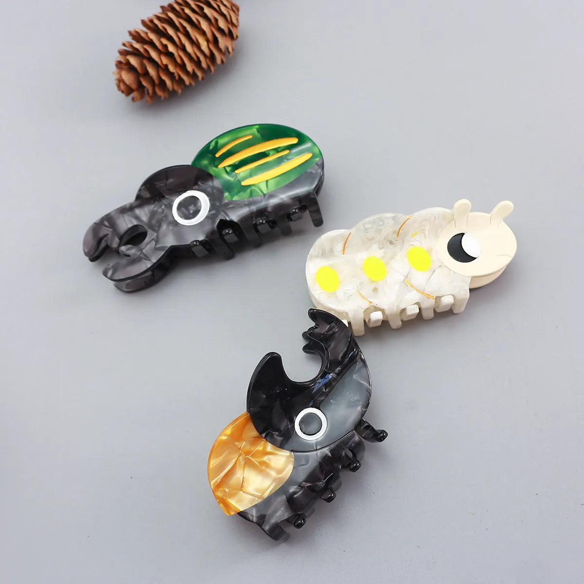 Handmade cartoon beetle grip brooch made from cellulose acetate in green, orange, or white insect designs.