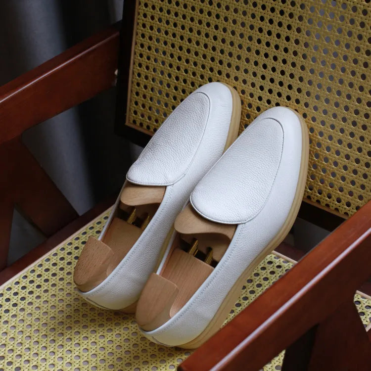 British handmade men's brown genuine leather flat loafers on a plain background.