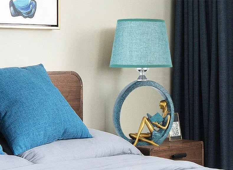 Blue resin reading girl table lamp with cloth shade on a table, 20x39.8cm
