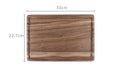 Black walnut wood chopping board with juice groove and side handle on kitchen counter