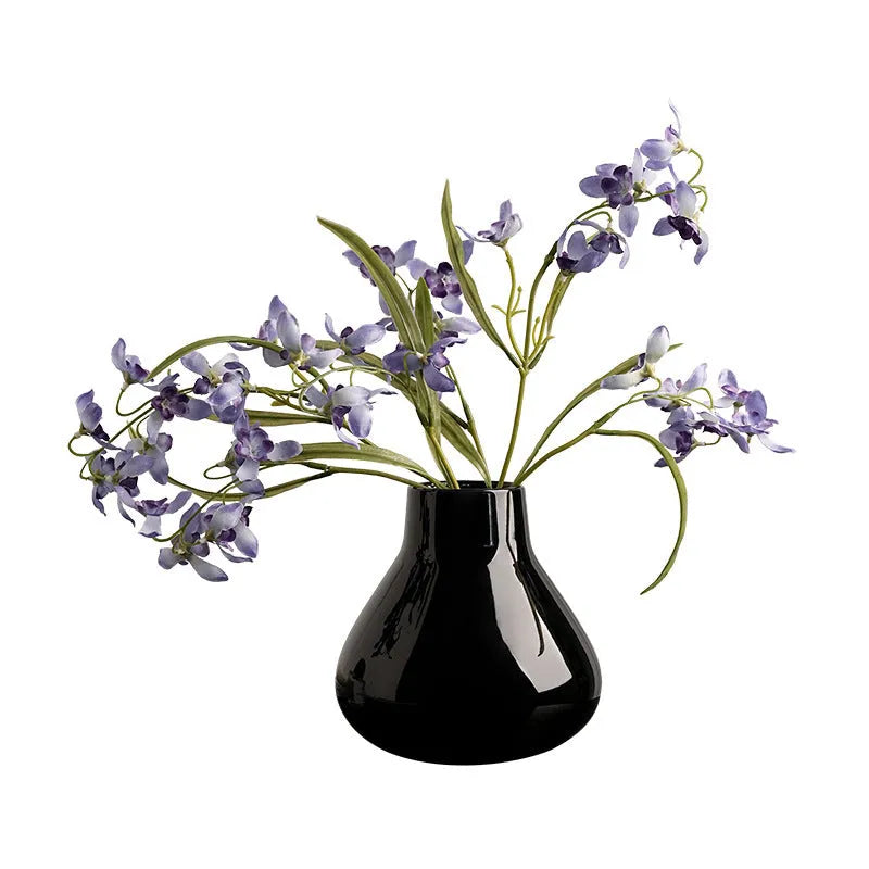 Black ceramic modern vase with white artificial orchid stems on wooden table