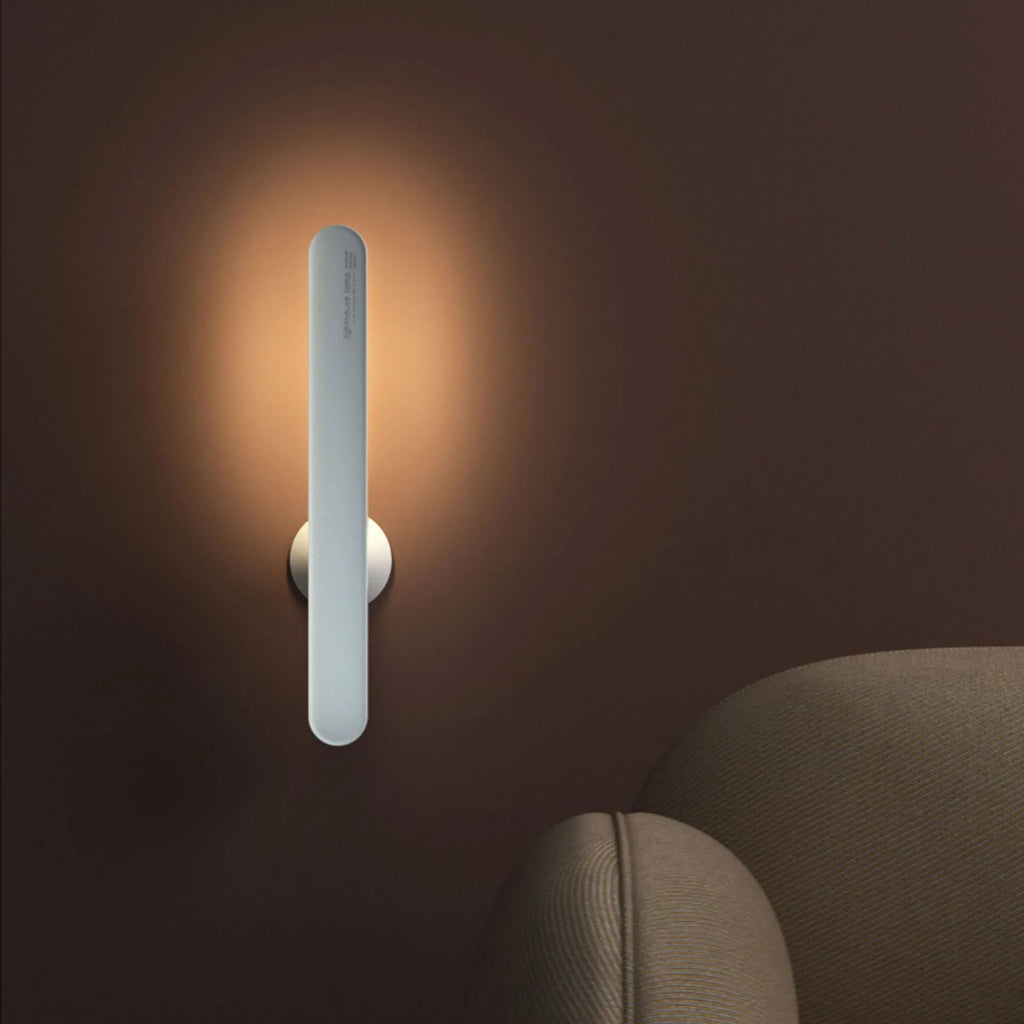 Geometric shaped white desk lamp with a magnetic base on a wooden table next to a book.