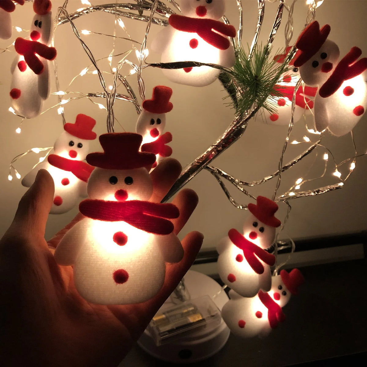 Close-up of warm white Christmas LED string lights with integrated snowman decoration on a green wire garland