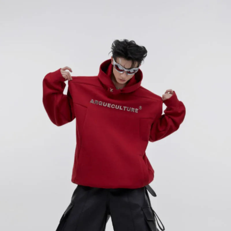 Man wearing a red loose-fit hooded sweater with a printed metal graphic design on the front.