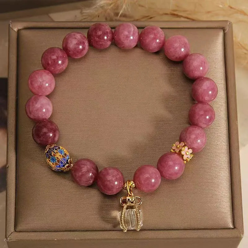 Close-up of a women's natural stone bracelet with a pink lotus tassel and pink white crystal electroplated flower pendant.