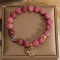 Close-up of a women's natural stone bracelet with a pink lotus tassel and pink white crystal electroplated flower pendant.