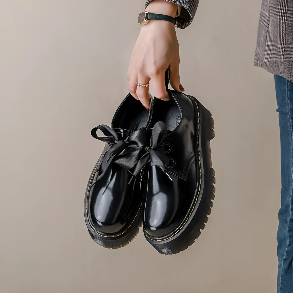 Black thick soled women's lace-up shoes with ribbon and cross strap details on a white background.