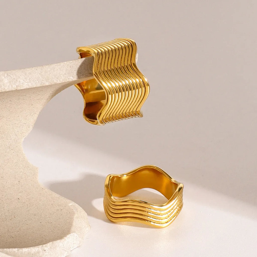 A geometric wide-band stainless steel ring with a wave design, shown in a polished silver tone.