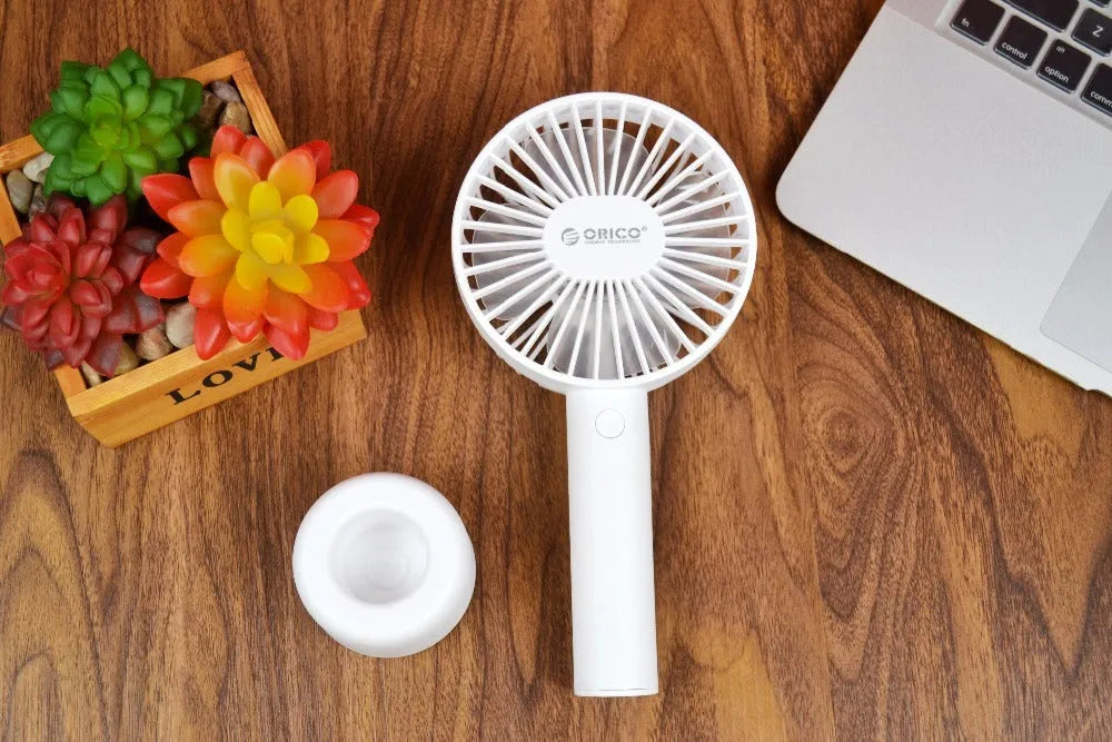 White ORICO FH1 handheld USB rechargeable desk fan with three-speed buttons on a desk.