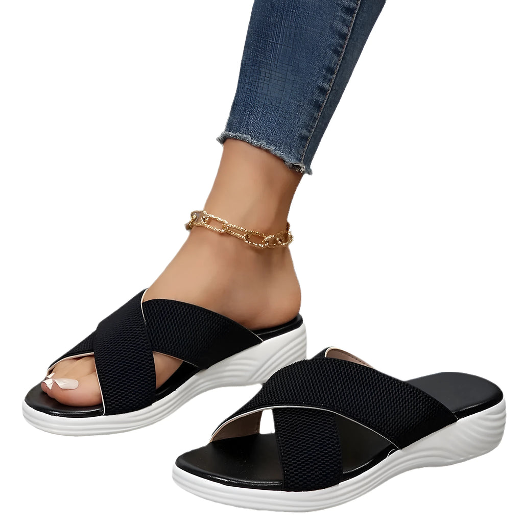 Black wedge slippers with peep toe and thick rubber sole on a grey background.