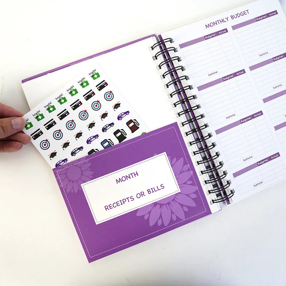 Purple coil-bound budget notebook with pen and stickers for financial planning