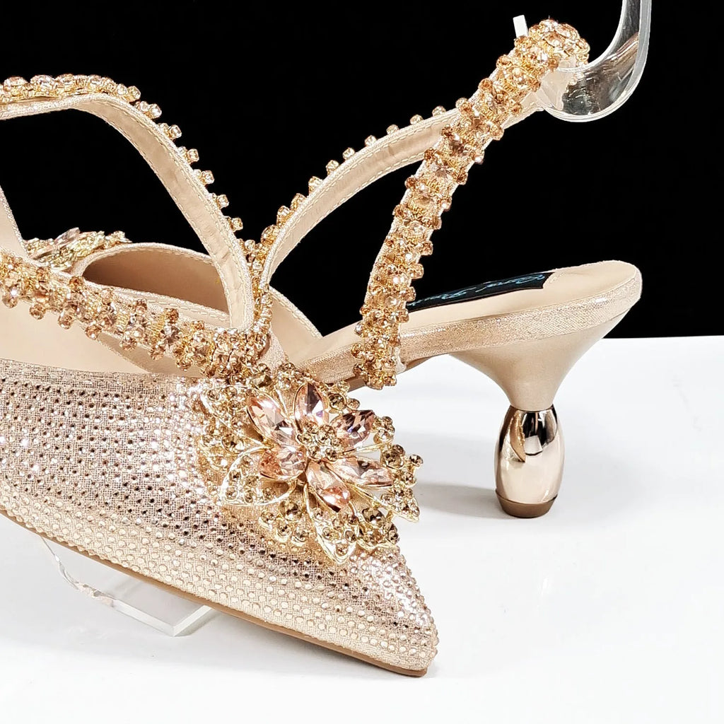 Women's black high heel ankle-strap sandals with floral buckle and chain detail next to matching clutch bag