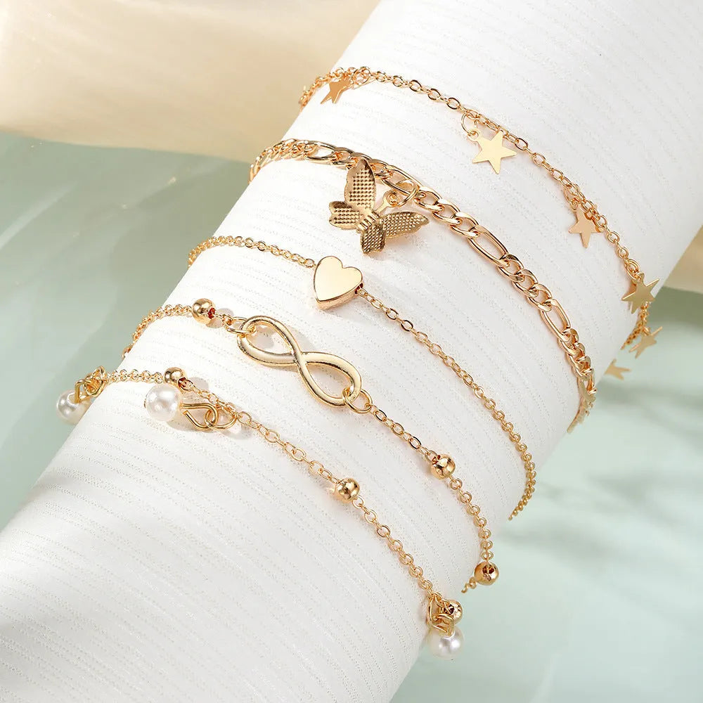 Set of four women's alloy anklets with butterfly, pearl, and heart charms.