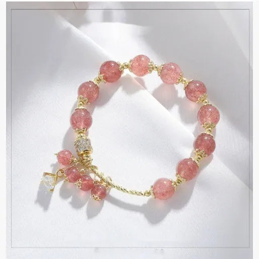 Close-up of a women's pink crystal bracelet with a heart-shaped Strawberry Quartz stone and a white pearl accent.
