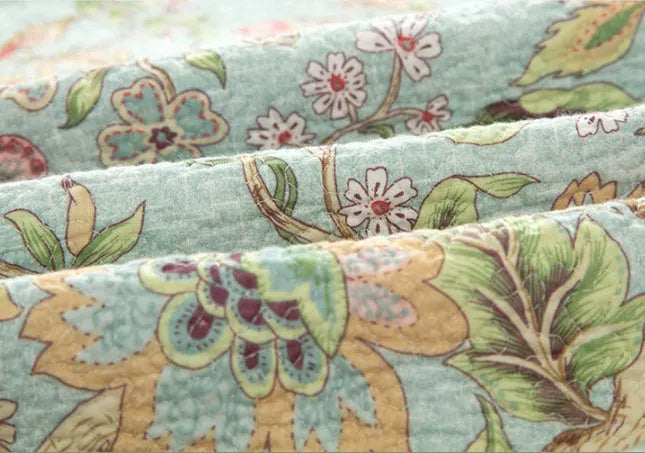 Blue botanical patterned quilted cotton bedspread set on a bed, showing plants, flowers, and bird design.