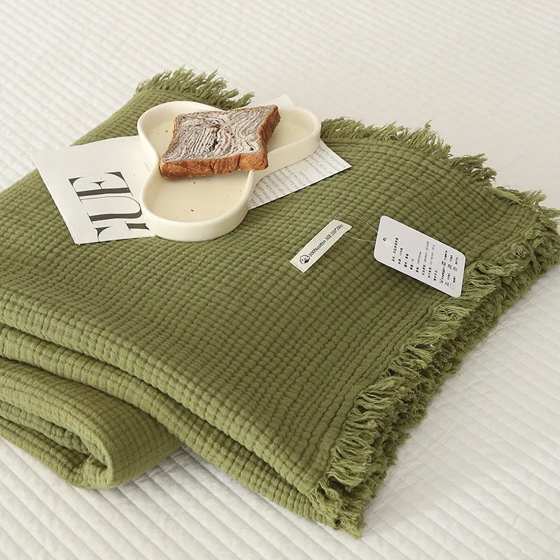 Cotton four-layer gauze blanket with tassel trim in avocado green colour on a chair.