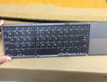 Black ultra-thin tri-fold Bluetooth keyboard with touchpad open and folded showing compatibility with iPhone and Android