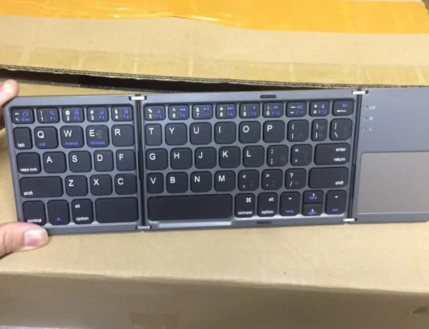 Black ultra-thin tri-fold Bluetooth keyboard with touchpad open and folded showing compatibility with iPhone and Android