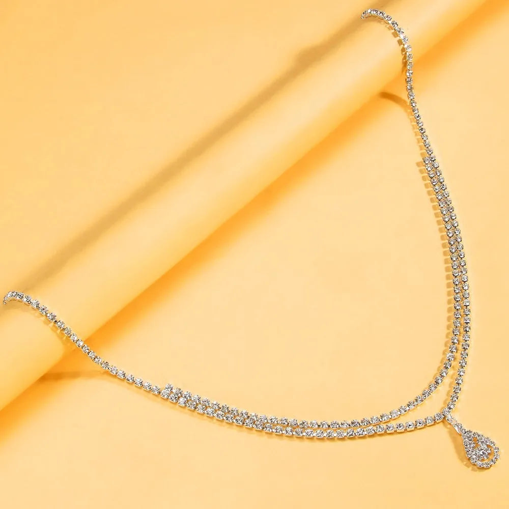 Gold coloured waist chain with a sparkling rhinestone water drop pendant and tassel details.