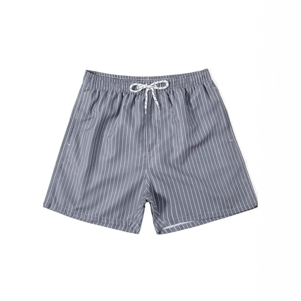 A man wearing grey striped polyester beach shorts with a straight leg opening, shown on a beach.