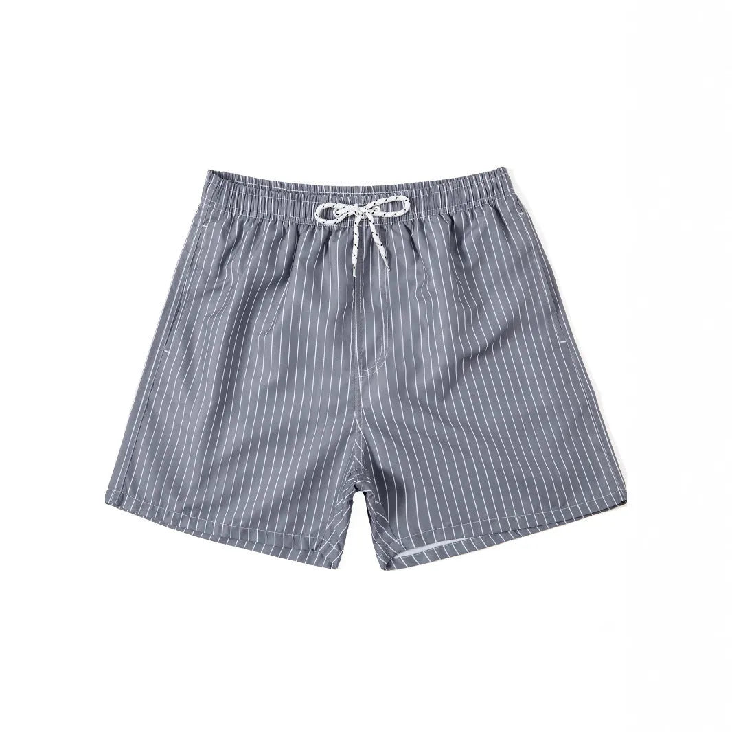A man wearing grey striped polyester beach shorts with a straight leg opening, shown on a beach.