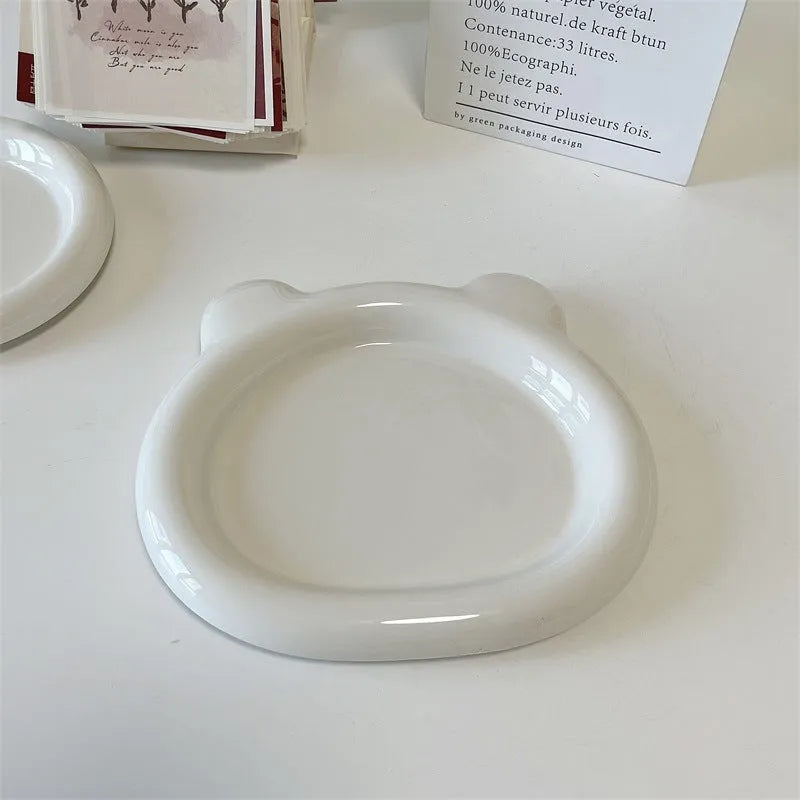 White porcelain plant saucer with a bear doodle design, shown next to a potted plant.