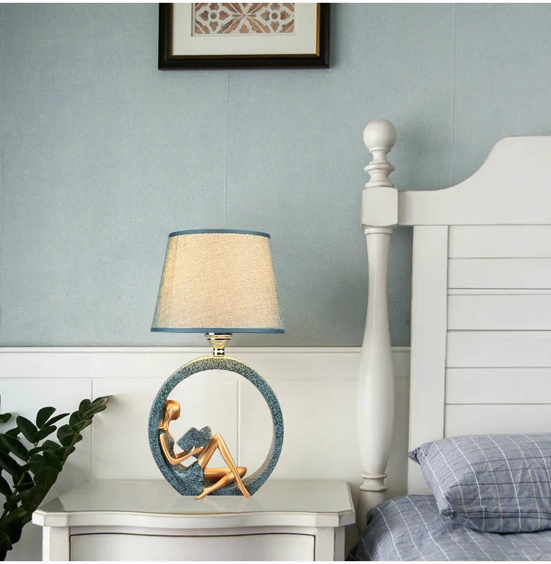 Blue resin reading girl table lamp with cloth shade on a table, 20x39.8cm