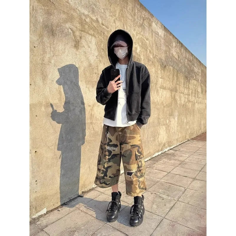 Man wearing loose fit camouflage print cropped jeans with ripped knees and patchwork details.
