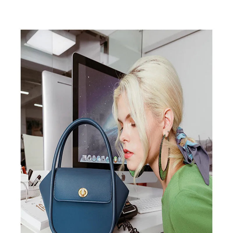 Women's winged leather handbag with cross-body strap in blue, showing latch closure and buckle detail.