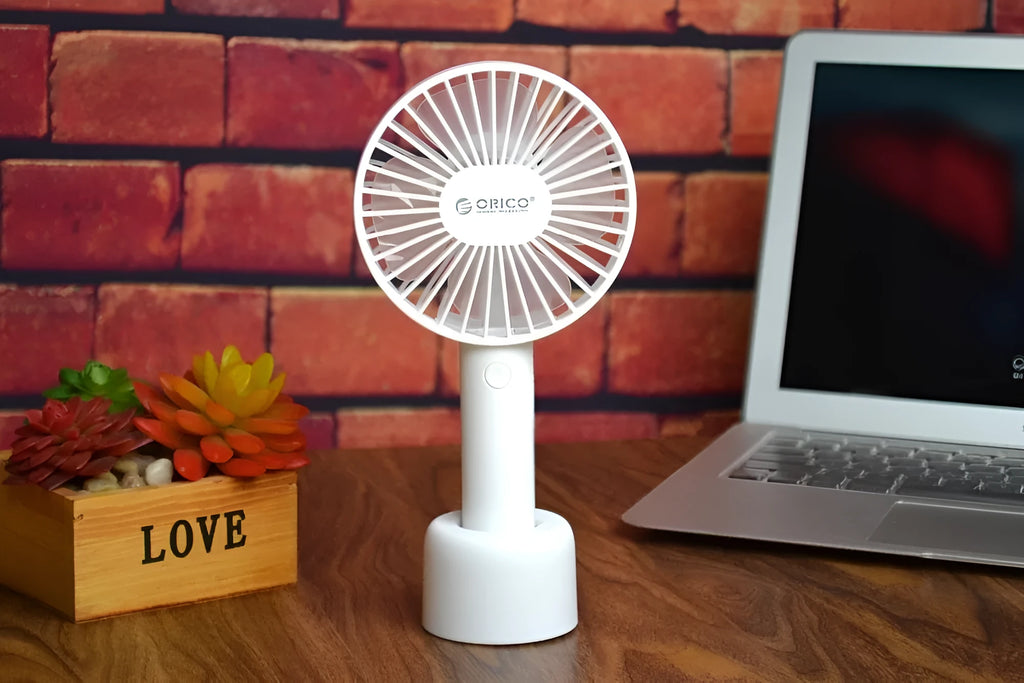 White ORICO FH1 handheld USB rechargeable desk fan with three-speed buttons on a desk.