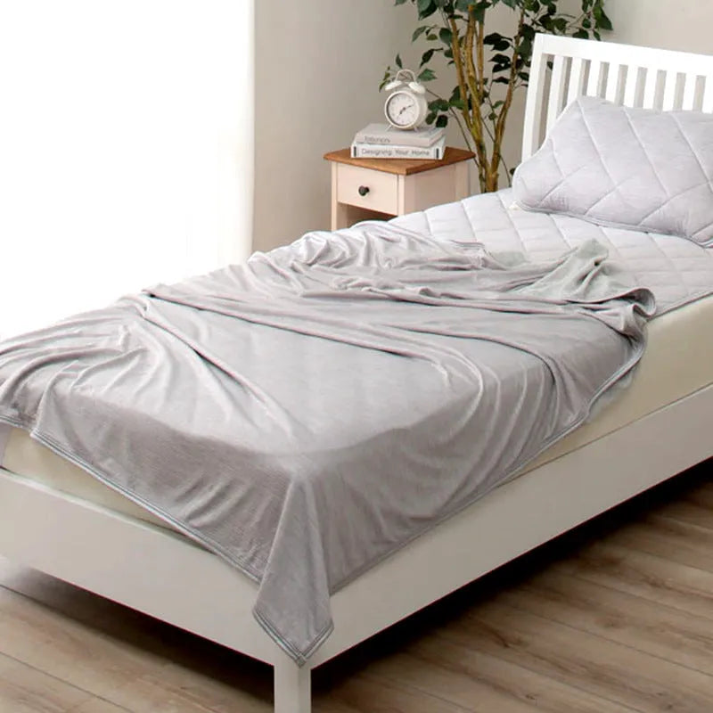 Blue cooling blanket with double-faced texture on a bed, showing its lightweight drape.