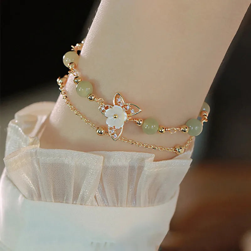 Yellow gold electroplated copper women's bracelet with geometric design showing butterfly and shell flower charms including Hetian jade elements
