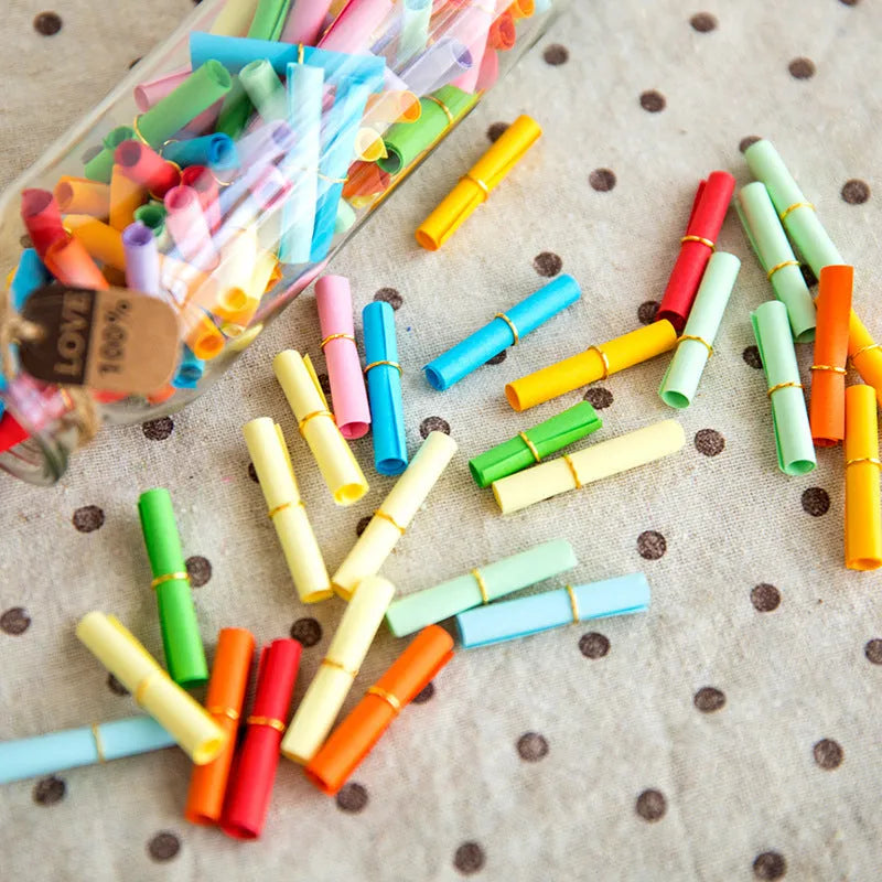 Coloured paper scrolls with metal eyelets in sizes 3x7cm, 4x7cm, 5x5cm, and 7x7cm for message writing.
