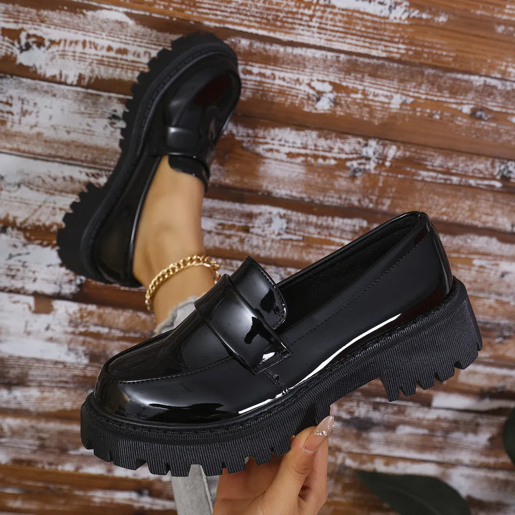 Women's black slip-on loafers with a chunky platform heel on a wooden floor