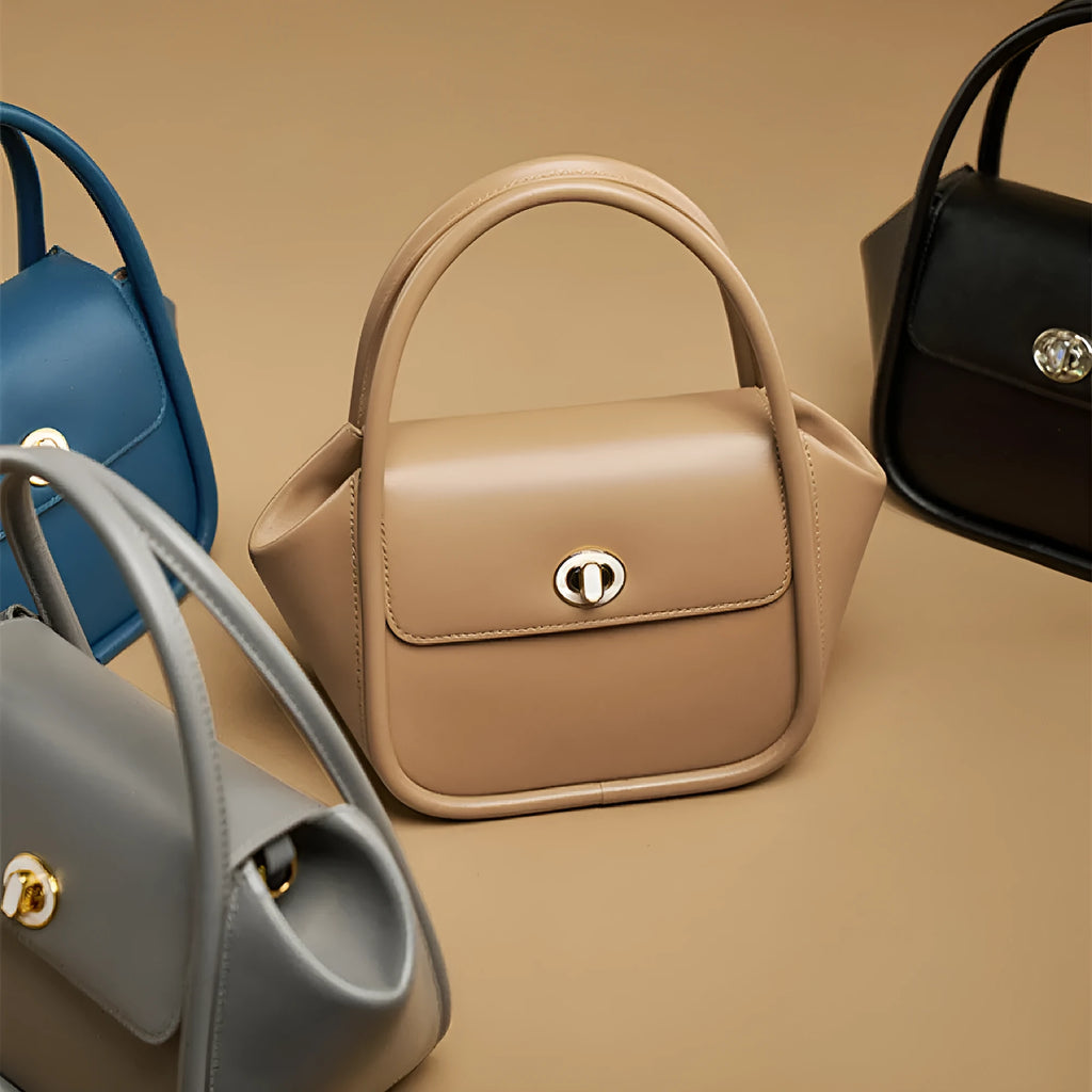 Women's winged leather handbag with cross-body strap in blue, showing latch closure and buckle detail.